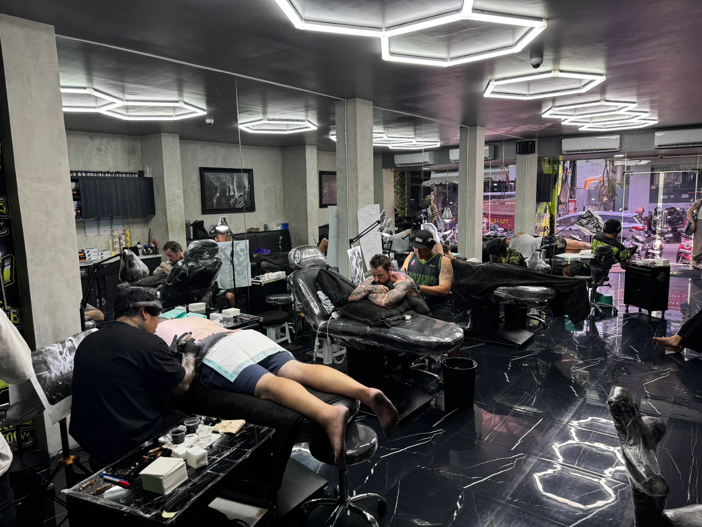 Appointment-only Bloodline Tattoo Bali studio with plastic-wrapped beds, hexagonal lighting, and artists in session
