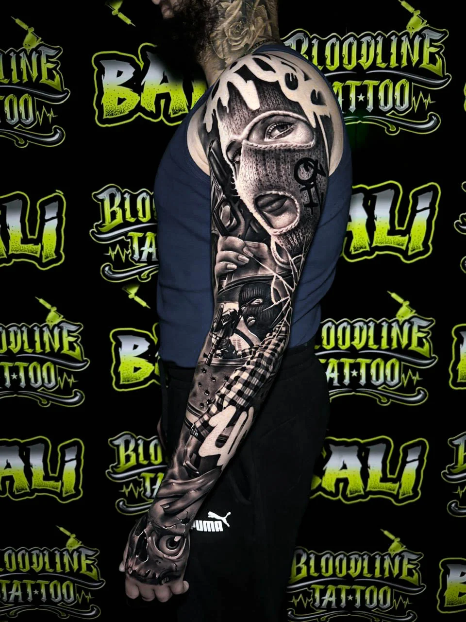 Detailed black and grey Chicano full arm sleeve tattoo featuring a masked woman, pistols, checkerboard patterns, and skull imagery at Bloodline Tattoo Bali.