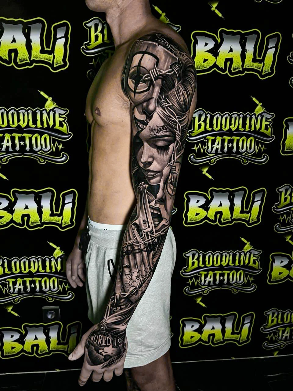 Detailed black and grey Chicano full arm sleeve tattoo featuring a woman portrait, barbed wire, scissors, spiderweb elements, and script at Bloodline Tattoo Bali.