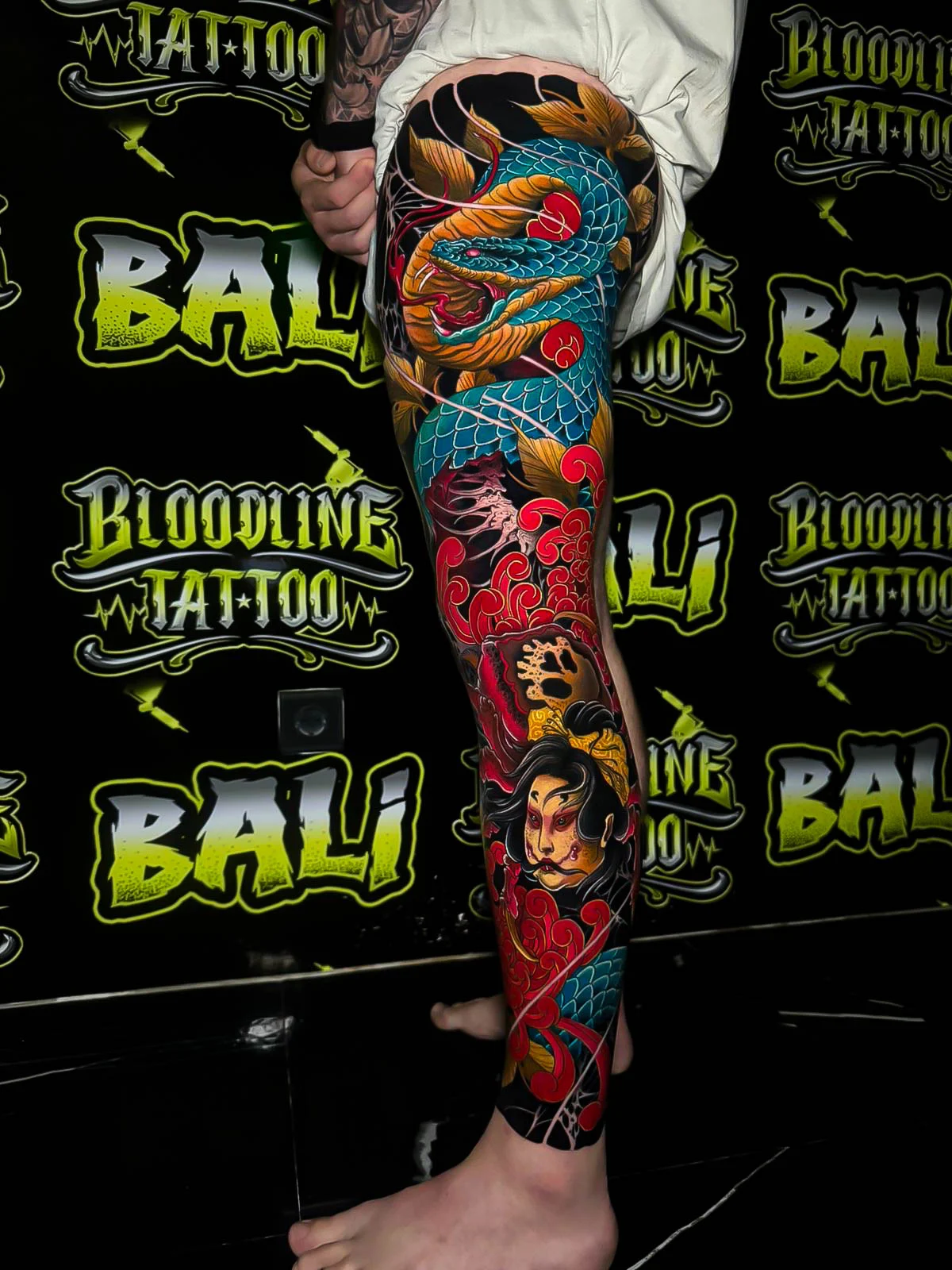Colour Japanese leg sleeve tattoo with a blue serpent, red cloud swirls, and a geisha portrait in rich traditional tones at Bloodline Tattoo Bali.