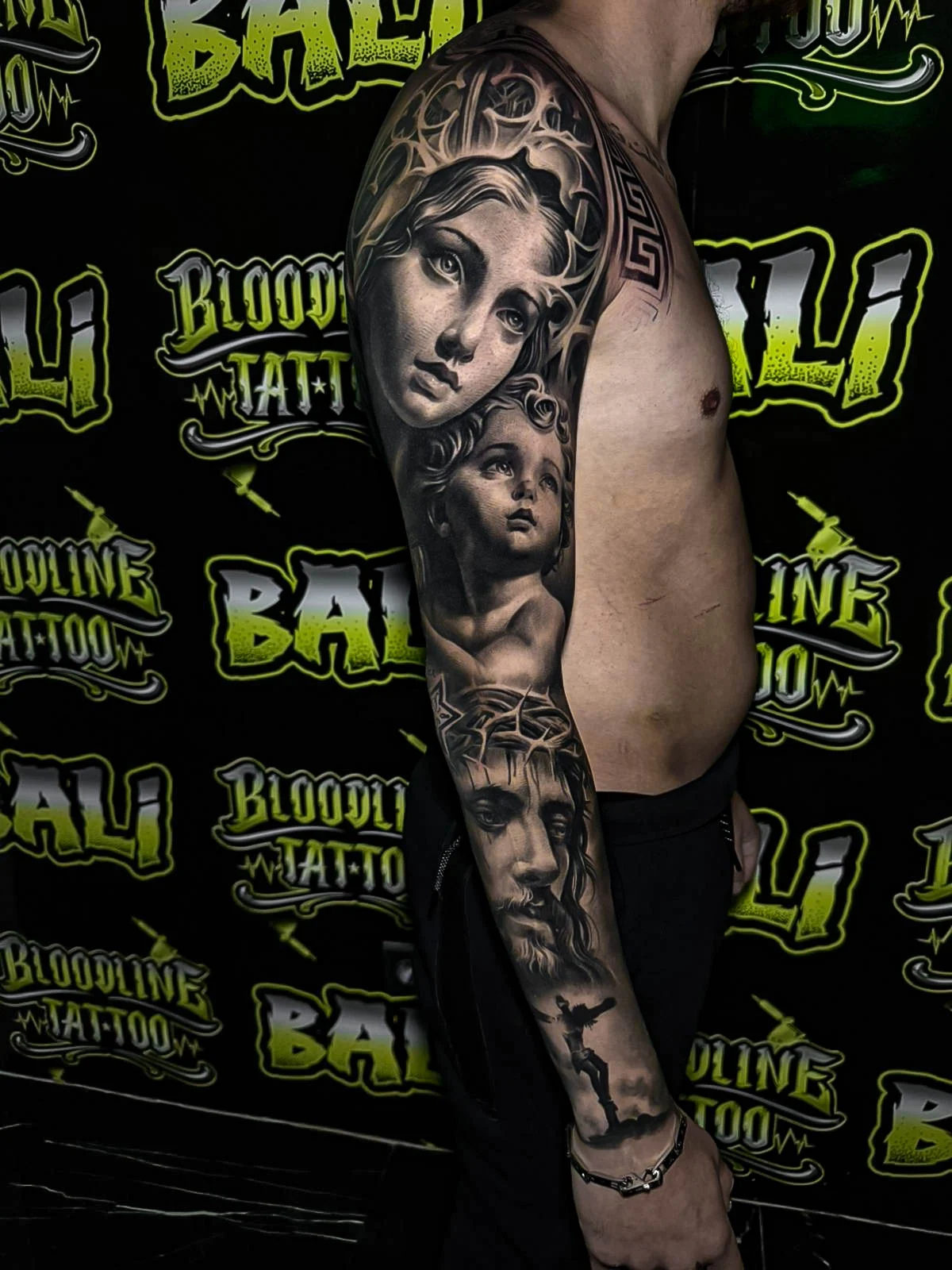 Healed black-and-grey sleeve with Madonna, cherub, and Christ portraiture, showing soft portrait realism and stable healed line integrity at Bloodline Tattoo Bali.