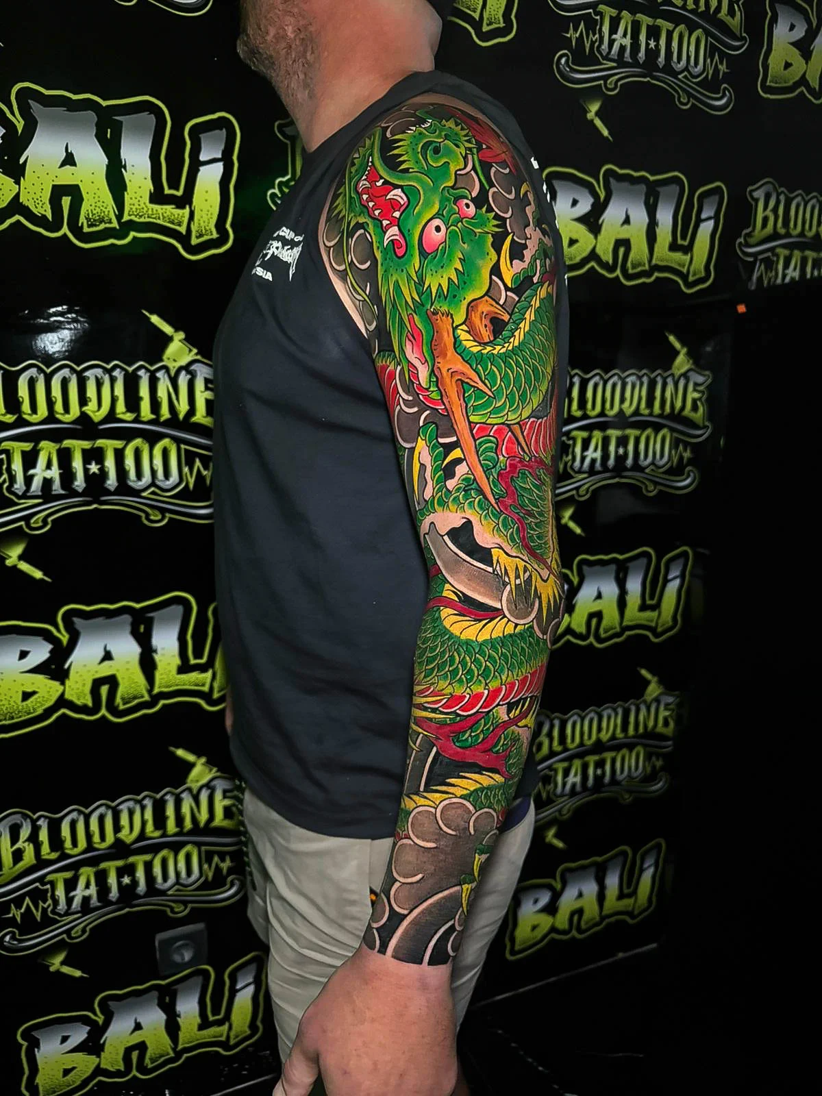 Japanese colour full sleeve with a bright green dragon, brown cloud bars, and red accents at Bloodline Tattoo Bali.