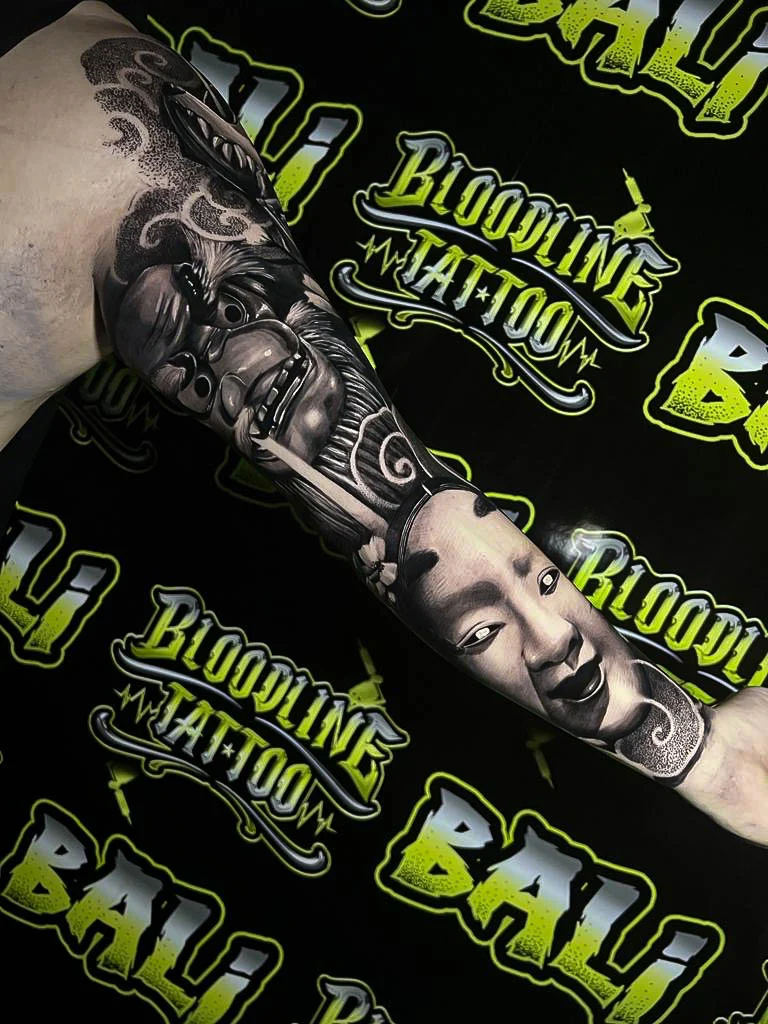 Black and grey Japanese arm tattoo with Hannya and Noh masks, cloud bars, and dotwork shading at Bloodline Tattoo Bali.