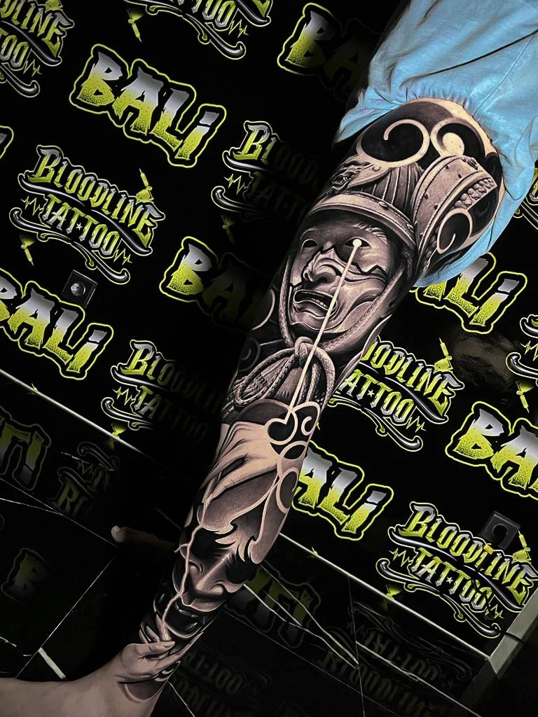 Black and grey Japanese full leg tattoo with a Hannya mask, samurai helmet, and flowing smoke at Bloodline Tattoo Bali.