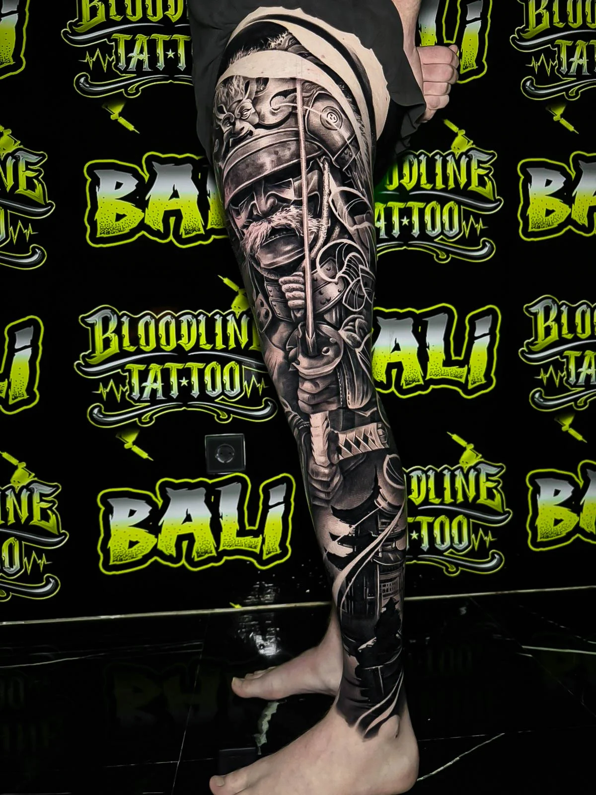 Black and grey Japanese full leg sleeve with a samurai warrior, drawn katana, and swirling smoke at Bloodline Tattoo Bali.