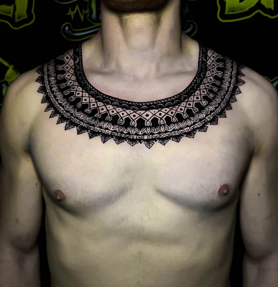 Ornamental chest collar tattoo with lace-like mandala borders, micro dotwork detail, and necklace-style symmetry across the clavicles at Bloodline Tattoo Bali.