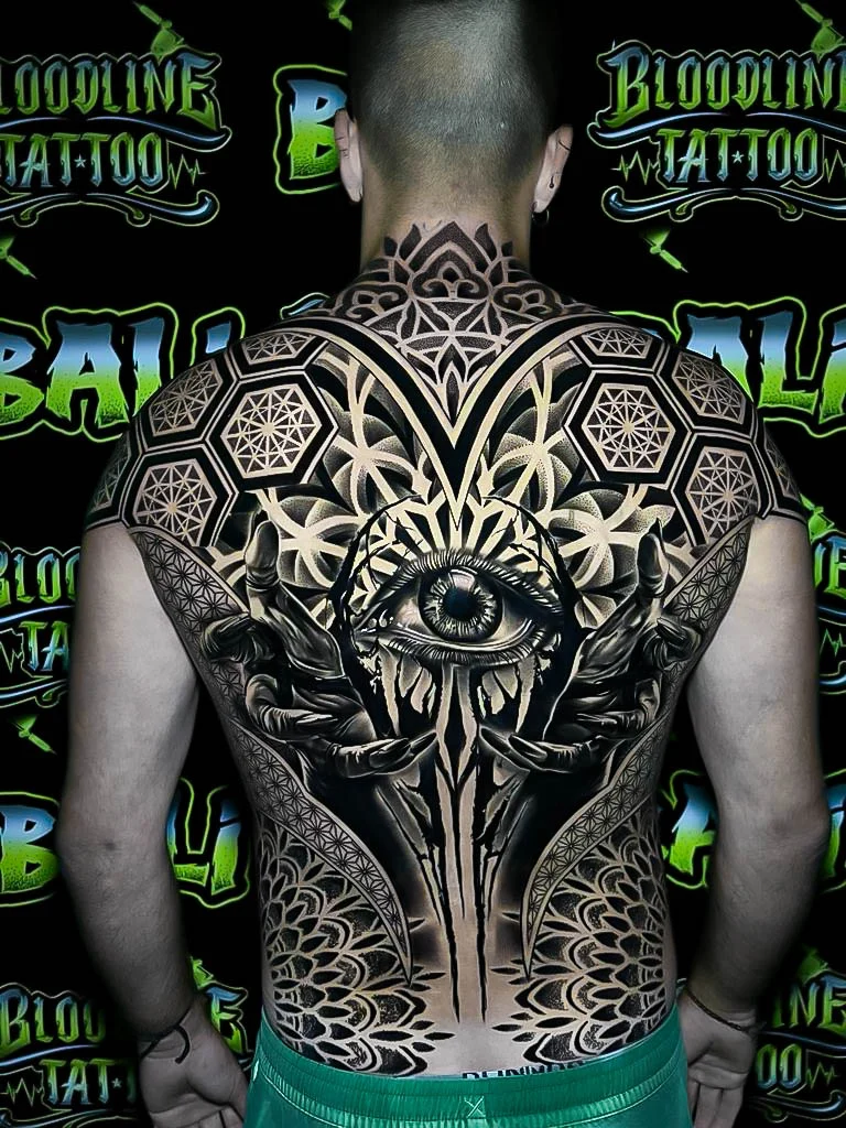 Full-back sacred geometry piece with an all-seeing eye, mirrored hands, hexagon fields, and petaled blackwork framing the spine at Bloodline Tattoo Bali.