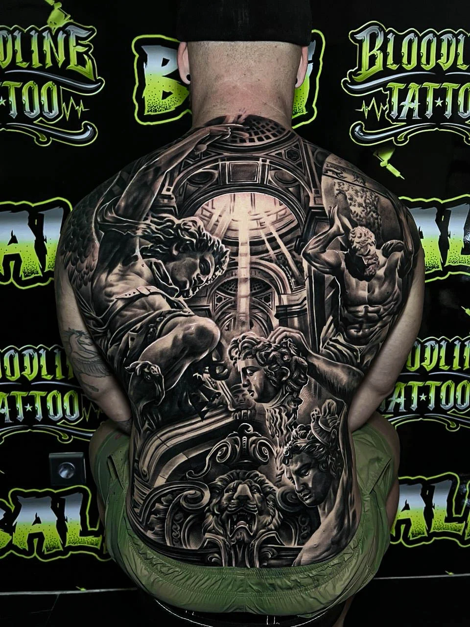 A black and grey realism full back piece with classical figures, cathedral arches, and dramatic light rays cutting through sacred imagery, at Bloodline Tattoo Bali.