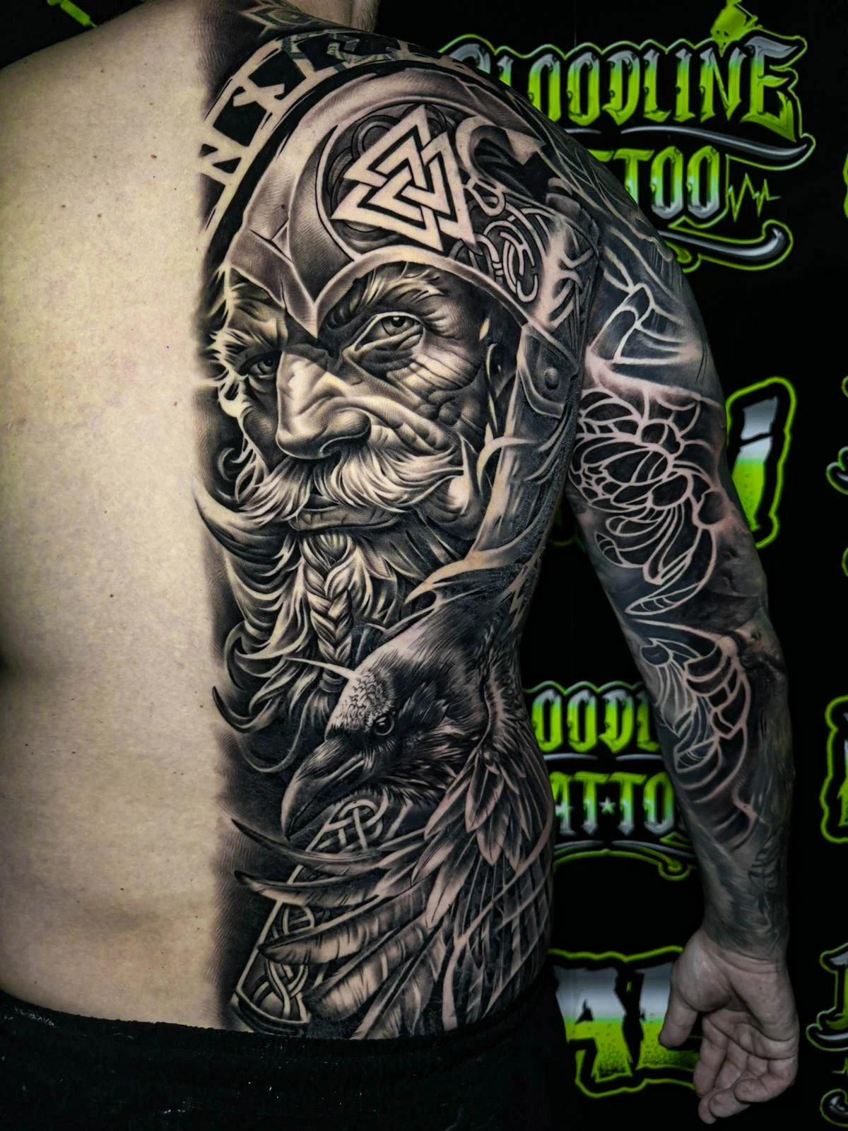 A black and grey realism arm sleeve of a Viking warrior portrait with braided beard detail, etched armor, and ornamental shading, at Bloodline Tattoo Bali.