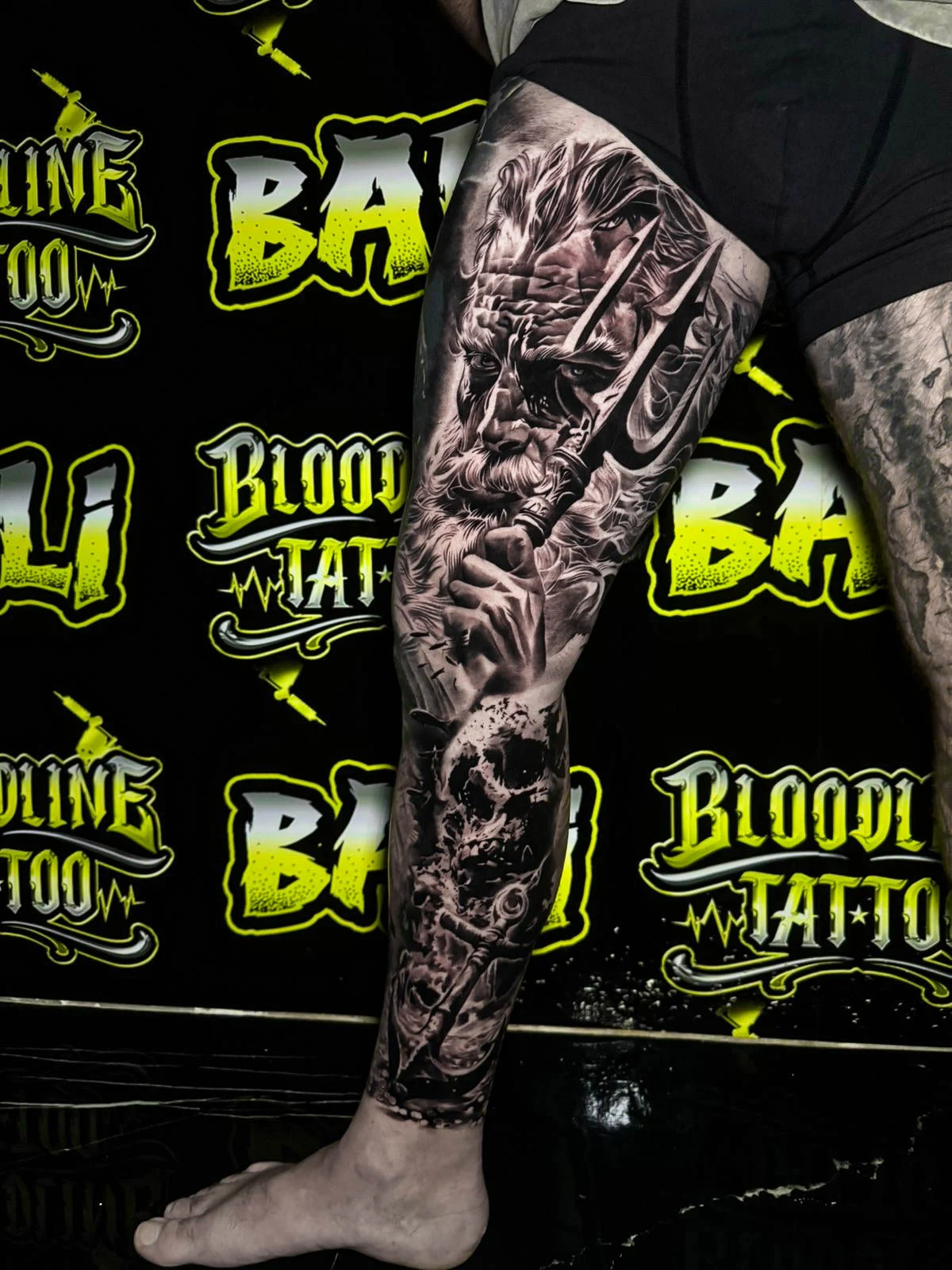 A black and grey realism lower leg sleeve with armored warrior imagery, mechanical detail, and dark shadowwork running down the calf, at Bloodline Tattoo Bali.